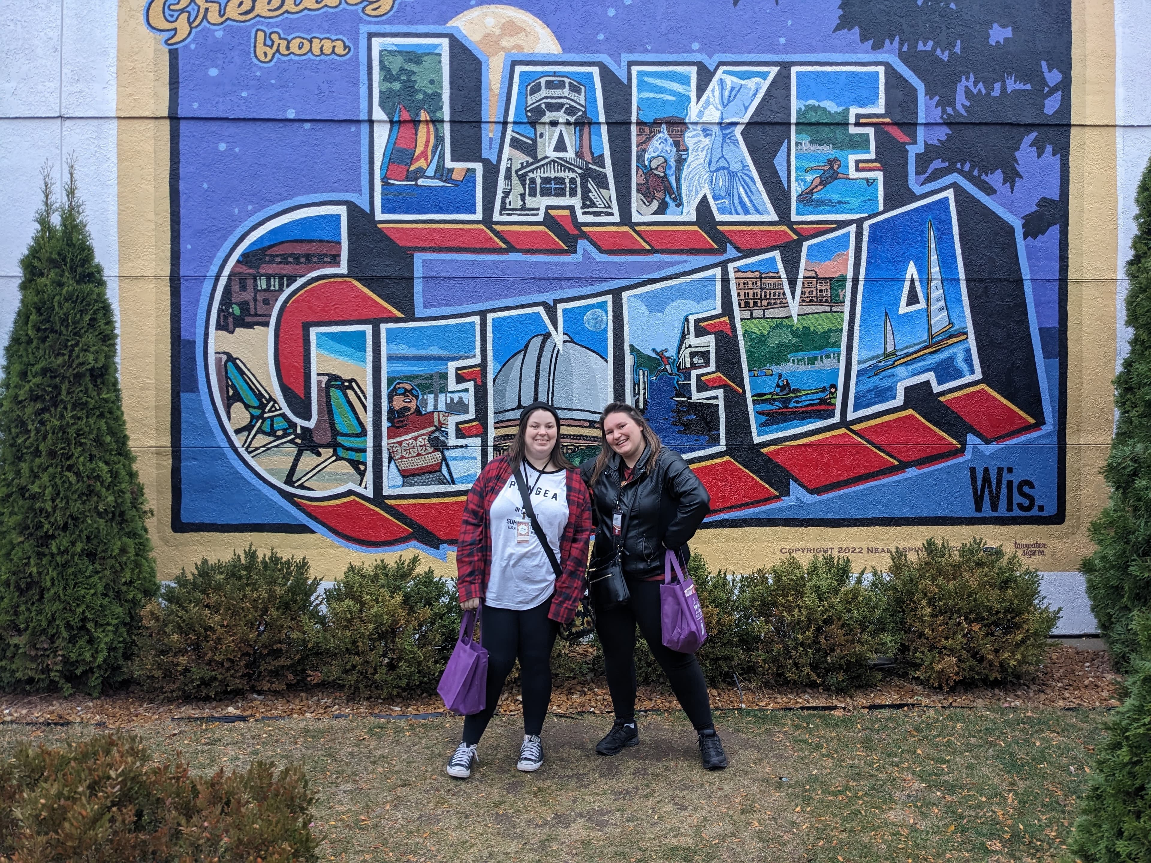 Two friends posing in front of the Greetings From Lake Geneva mural downtown
